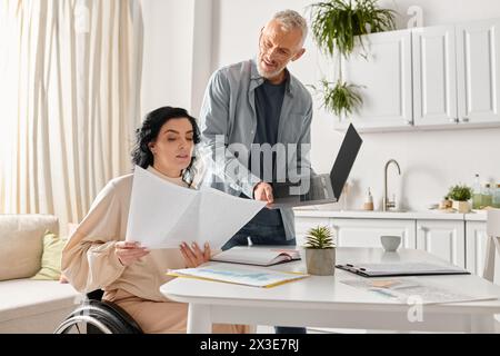 A disabled woman in a wheelchair and her husband collaborate on paperwork in their kitchen at home. Stock Photo