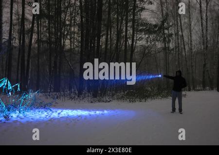 Man with electric torch stands in dark night forest during blizzard at winter Stock Photo