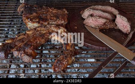Argentine barbecue. Some excellent pieces of Argentinian beef on a charcoal grill and an a wooden table with knife. Close-up view of sliced grilled be Stock Photo