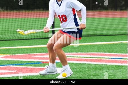 High school female lacross player ready to pick up the ball during a game on a turf field. Stock Photo