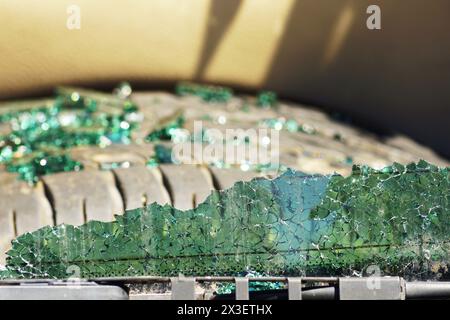 A cracked rear window of a car and glass shards lying on a spare tire in the background Stock Photo