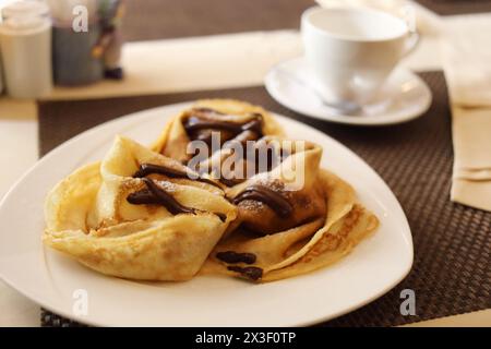 Pancakes with chocolate on plate on table with serving in cafe Stock Photo
