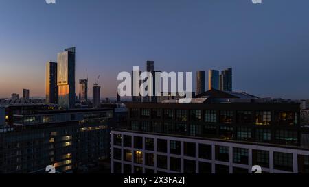 A serene twilight view over a cityscape showcasing glowing skyscraper windows against a dusky sky, reflecting the bustling city life within Stock Photo