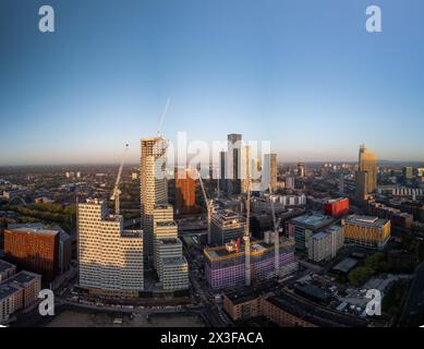 An aerial view capturing a modern city's high-rise buildings and construction cranes bathed in the warm glow of the setting sun Stock Photo