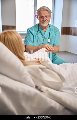 Male doctor supporting lady patient on hospital bed Stock Photo