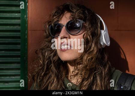 Young Latin American woman with curly hair wearing headphones in the street Stock Photo
