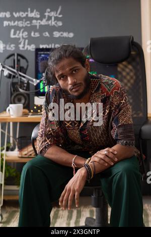 Young tired musician with wrinkles on forehead looking at camera with troubled expression while sitting in armchair by workplace Stock Photo
