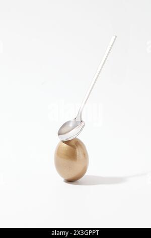 Minimal scene of a golden Easter egg and a spoon decorated against white background. Easter commemorates the resurrection of Jesus Christ, three days Stock Photo