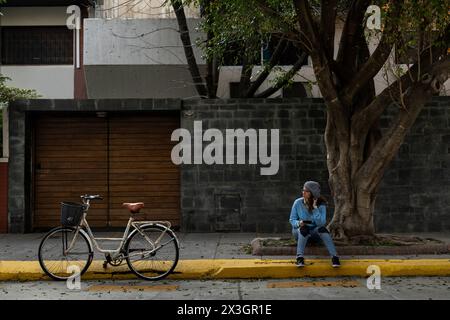 Young Latin American hipster woman sitting on the sidewalk in front of her house Stock Photo