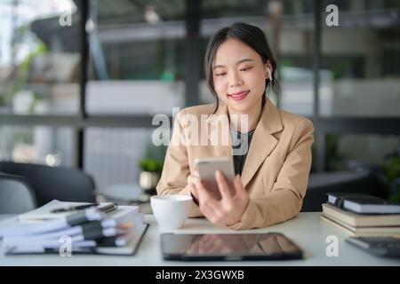 Businesswomen wearing bluetooth headphones and using smartphone to meeting on video call about financial and investment data of new business while dis Stock Photo