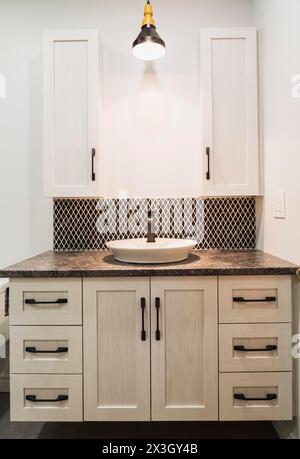 Antique finish wooden cabinet with black nuanced laminated countertop and ceramic backsplash in bathroom inside contemporary home, Quebec, Canada Stock Photo