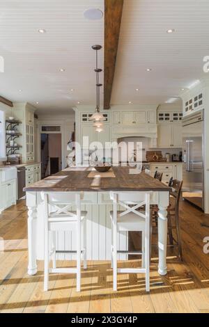 White painted maple wood antique style cabinets with tan coloured quartz countertops, island with brown stained wood plank countertop and high back Stock Photo