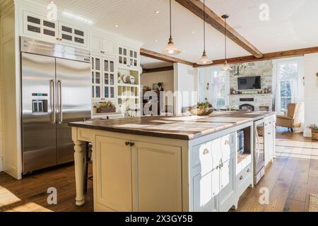 White painted maple wood antique style cabinets with tan coloured quartz countertops, island with brown stained wood plank countertop and high back Stock Photo