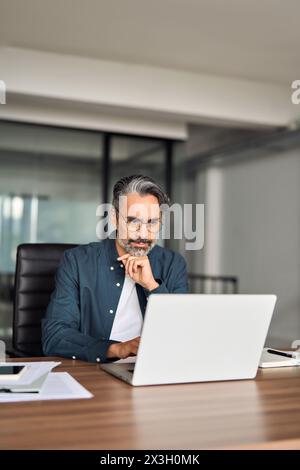 Busy serious middle aged business man sitting at desk using laptop computer. Stock Photo