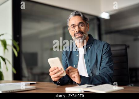 Older business man sitting at office desk using mobile phone. Portrait. Stock Photo