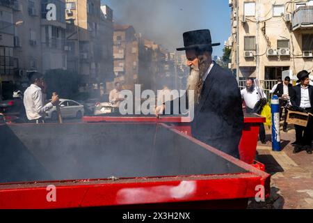 April 22, 2024, Bnei Brak, Israel: A Jewish man throws leaven into the fire during the Biur Chametz. During the Biur Chametz, religious Jews fulfill their obligation to inspect their homes for any leaven and eliminate it before the night of Passover. In ultra-Orthodox cities in Israel, fires are set up in major locations in the city for this purpose, where people bring their bread leftovers to burn the leaven. During the seven days of Passover, they are prohibited from eating or possessing any leaven, symbolizing the dough the Israelites did not have time to allow to rise before the Exodus fro Stock Photo