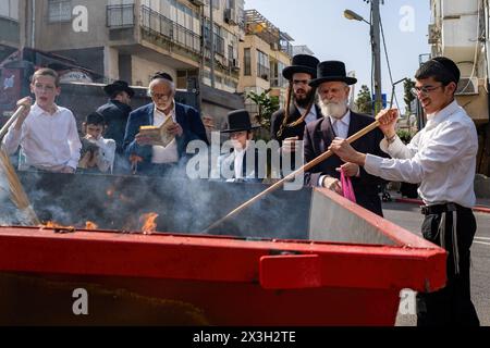 April 22, 2024, Bnei Brak, Israel: A Jewish man throws leaven into the fire during the Biur Chametz. During the Biur Chametz, religious Jews fulfill their obligation to inspect their homes for any leaven and eliminate it before the night of Passover. In ultra-Orthodox cities in Israel, fires are set up in major locations in the city for this purpose, where people bring their bread leftovers to burn the leaven. During the seven days of Passover, they are prohibited from eating or possessing any leaven, symbolizing the dough the Israelites did not have time to allow to rise before the Exodus fro Stock Photo
