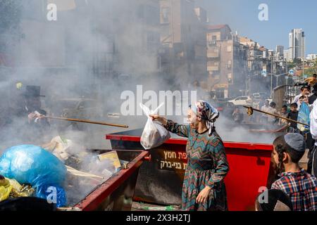 April 22, 2024, Bnei Brak, Israel: A Jewish woman throws leaven into the fire during the Biur Chametz. During the Biur Chametz, religious Jews fulfill their obligation to inspect their homes for any leaven and eliminate it before the night of Passover. In ultra-Orthodox cities in Israel, fires are set up in major locations in the city for this purpose, where people bring their bread leftovers to burn the leaven. During the seven days of Passover, they are prohibited from eating or possessing any leaven, symbolizing the dough the Israelites did not have time to allow to rise before the Exodus f Stock Photo