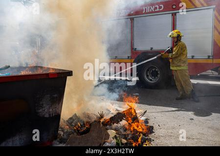 April 22, 2024, Bnei Brak, Israel: A firefighter puts out a fire lit outside of the designated area. During the Biur Chametz, religious Jews fulfill their obligation to inspect their homes for any leaven and eliminate it before the night of Passover. In ultra-Orthodox cities in Israel, fires are set up in major locations in the city for this purpose, where people bring their bread leftovers to burn the leaven. During the seven days of Passover, they are prohibited from eating or possessing any leaven, symbolizing the dough the Israelites did not have time to allow to rise before the Exodus fro Stock Photo