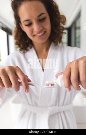 Caucasian woman in robe applying toothpaste, smiling gently Stock Photo