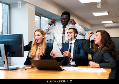 Multiracial office team celebrates success at work with high fives. Excited colleagues enjoy victory in corporate environment, happy faces around Stock Photo