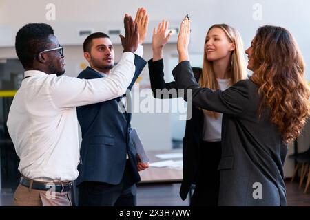 Multiethnic business team celebrates success with five in modern office setting. African, Arabic, Asian, Caucasian colleagues enjoy victory moment Stock Photo