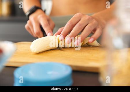A young Caucasian woman slicing banana on cutting board at home Stock Photo