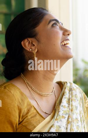 Indian young woman wearing traditional saree, looking up with smile at home Stock Photo