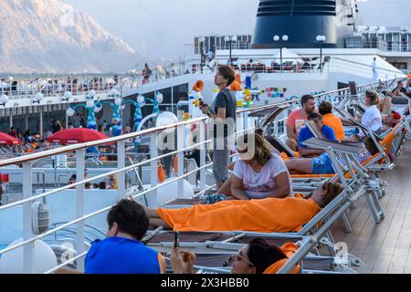 Hasab, Oman - 1 January 2024: A tranquil scene unfolds as tourists enjoy a serene sunset from the deck of a cruise ship docked at Hasab Port, with the Stock Photo