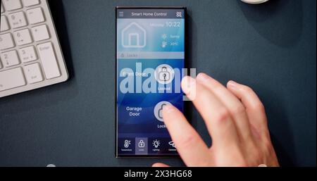 Hand Using Mobile Phone With Home Control System On Screen Stock Photo