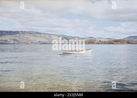 A person rows a wooden rowing boat across the waters of Loch Lomond in Argyll, Scotland on a sunny, calm day. Stock Photo