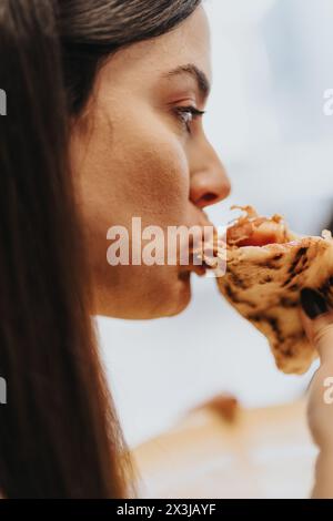 A beautiful brunette woman takes a bite of pizza, enjoying a work break with friends in a pleasant atmosphere. Stock Photo