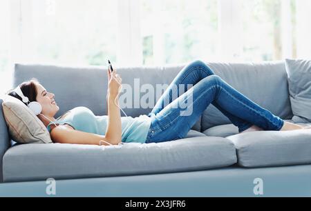 Girl, headphones and smartphone on sofa in house for music, relax and self care on study break. Woman, headset and phone on couch in home lounge for Stock Photo