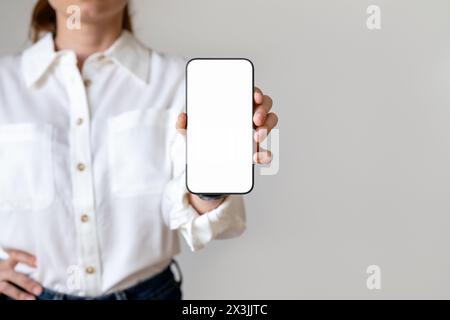 Businesswoman in a white shirt shows the screen of her smartphone to the camera. Mockup of blank screen of mobile phone in hand of female businesspers Stock Photo