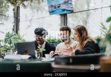 A multicultural group of business people engages in a collaborative discussion around a laptop in a restaurant with a lush, green ambiance. Stock Photo
