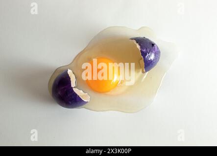 Cracked purple eggshell with raw egg. Creative copy space on light background. Minimal Easter concept. Stock Photo