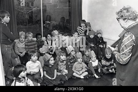 1970s, historical, inside a living room in a house, a young childrens party, an elderly lady relative getting the group of young boys and girls attention by holding up a picture book. Stock Photo