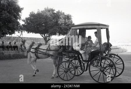 1960s, historical, a mature couple with their grandchild sitting in a horse drawn tourist carriage, No 49 on side lamp, Malta. Known as karrozzin, these horse and carriages as a form of transport date back to the 1850s. Stock Photo