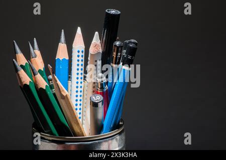 Small assortment of pencils standing vertically in a tin can against a dark background. Stock Photo