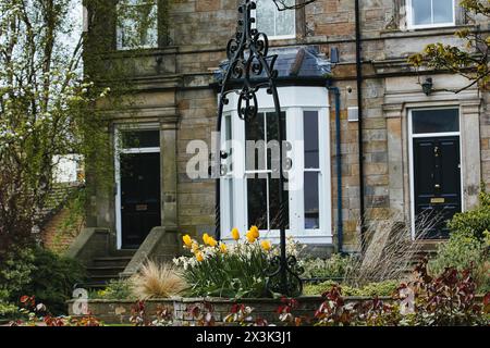 A charming old house with a decorative iron lamp post in the foreground, surrounded by blooming flowers and lush greenery. Stock Photo