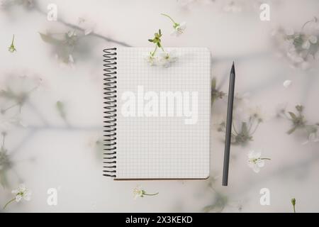 Guest list. Notebook, pencil and beautiful cherry tree blossoms on spring floral background, flat lay Stock Photo