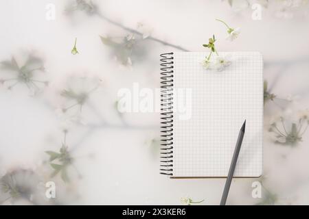 Guest list. Notebook, pencil and beautiful cherry tree blossoms on spring floral background, flat lay. Space for text Stock Photo