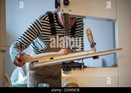 Focused man carpenter working on lathe cutting wooden block with special machine in wood workshop. Stock Photo