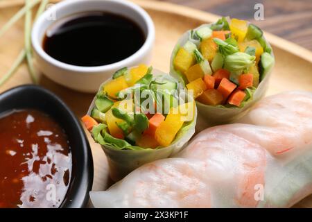 Tasty spring rolls and sauces on wooden plate, closeup Stock Photo