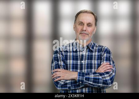 Portrait of a handsome mature man with folded arms standing in office. Checkered windows background. Stock Photo