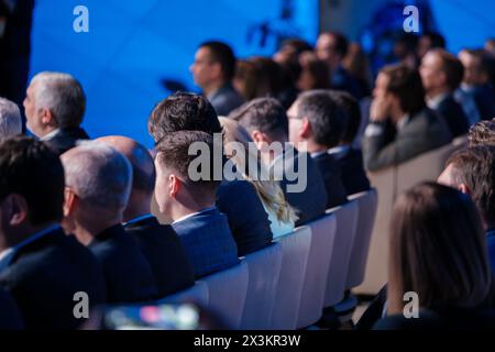 Professionally dressed audience members at a corporate event are focused on a presentation, illustrating engagement and professional development in a business setting. Stock Photo