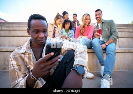 Serious black guy using smart phone. African American man holding cell outdoor with friends Stock Photo