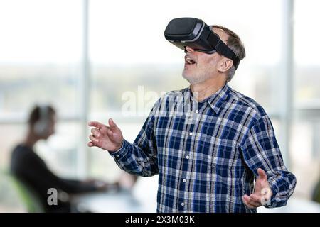 Excited elder man wearing vr headset with his mouth open. Indoor office enviroment background. Stock Photo