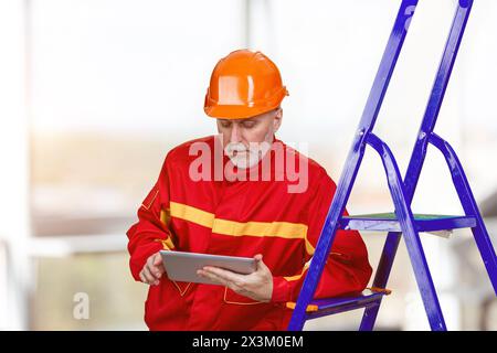 Happy male factory manager using digital tablet in warehouse. Worker wearing red robe and orange helmet. Stock Photo