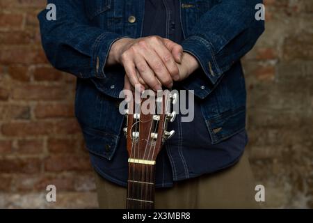 Medium shot of adult male hands on the headstock of a classical guitar. Concept of music and stringed instruments Stock Photo